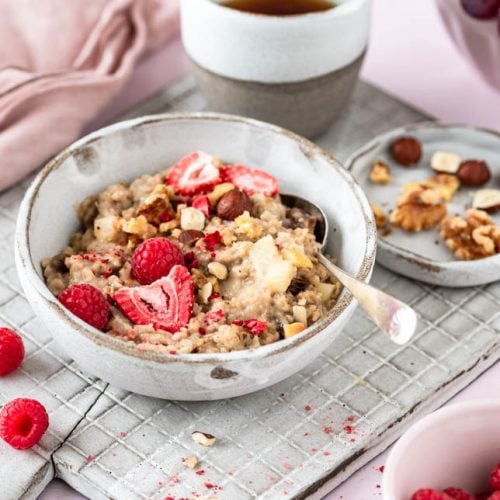 Eine Bowl mit Porridge mit Beeren und Nüssen auf Brett.