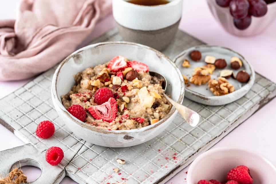 Eine Bowl mit Porridge mit Beeren und Nüssen auf Brett.