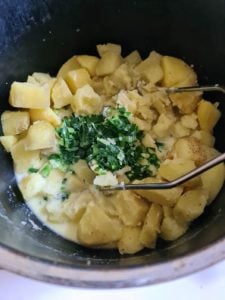 Kartoffelwürfel mit Bärlauch in Topf und einem Stampfer.