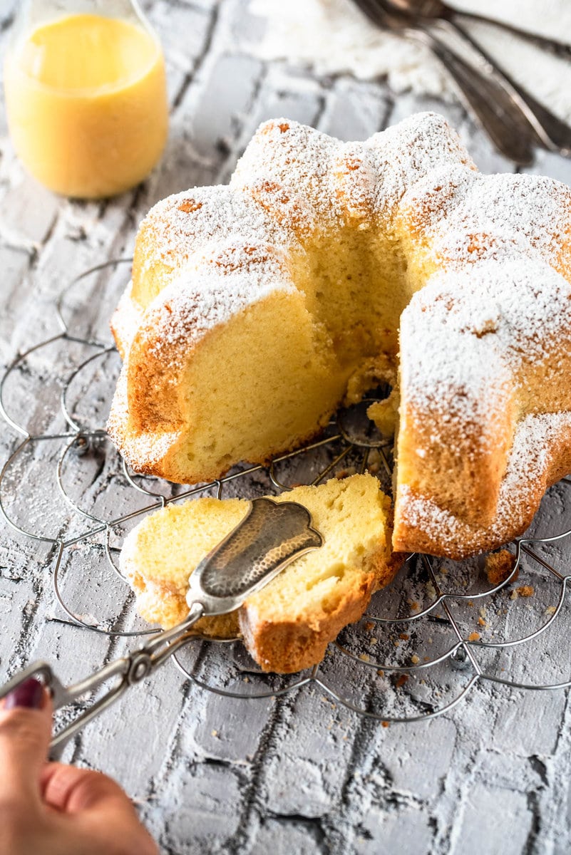 Eine Hand nimmt mit einer Kuchenzange ein Stück Kuchen
