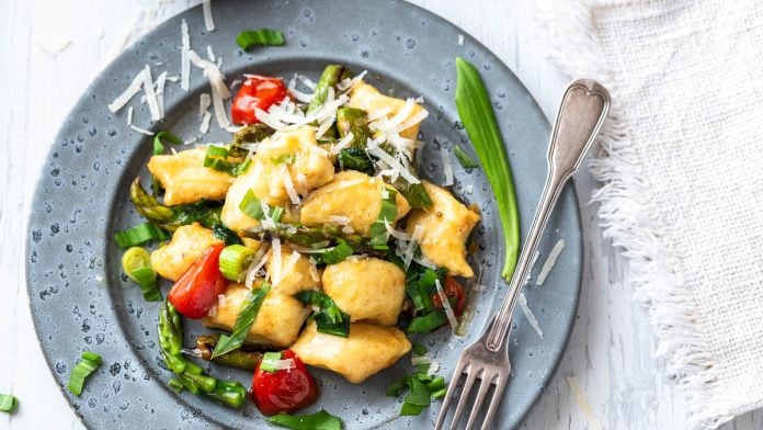 Ein Teller Gnocchi mit Spargel, Bärlauch und Tomaten mit Gabel.