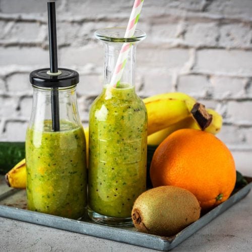 Zwei Flaschen mit grünem Getränk und Obst.