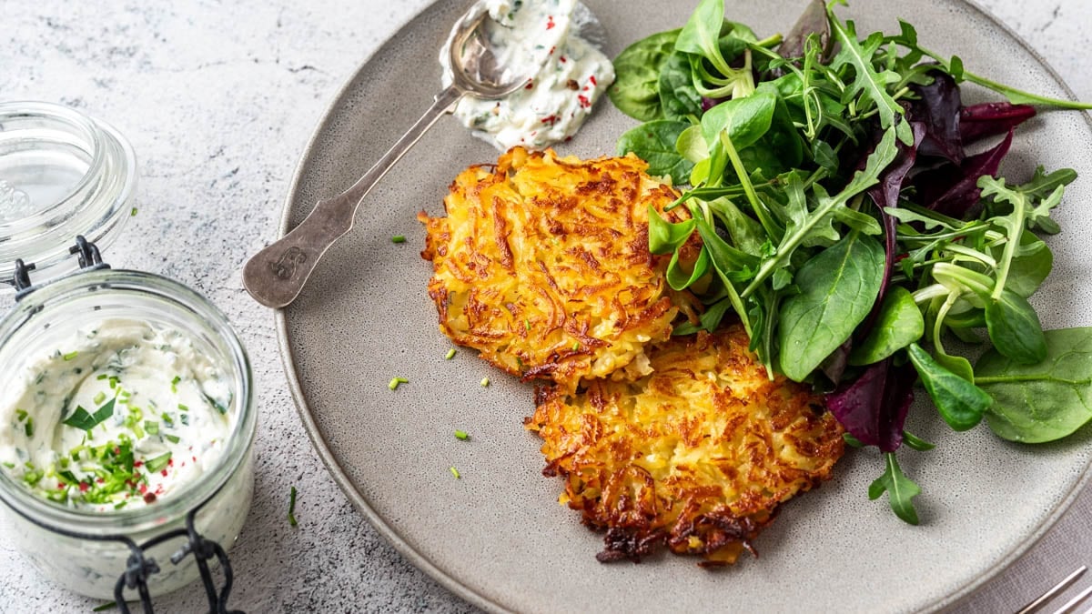 Knusprige Kartoffelrösti aus gekochten Kartoffeln mit Kräuterquark und frischem Salat auf einem Teller