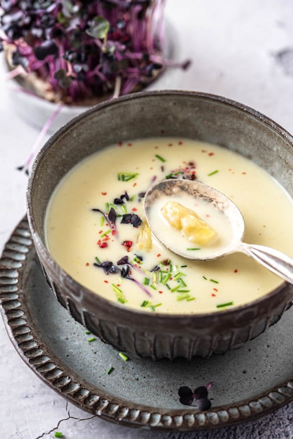 Eine Hand hält Löffel über Spargelsuppe