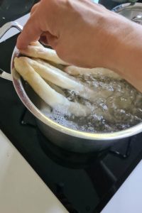 Eine Hand drückt Spargelstangen in kochendes Wasser