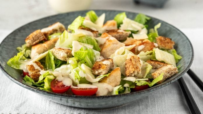 Eine Bowl Caesar Salad mit Hühnchen, Croutons und Dressing