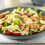 Eine Bowl Caesar Salad mit Hühnchen, Croutons und Dressing