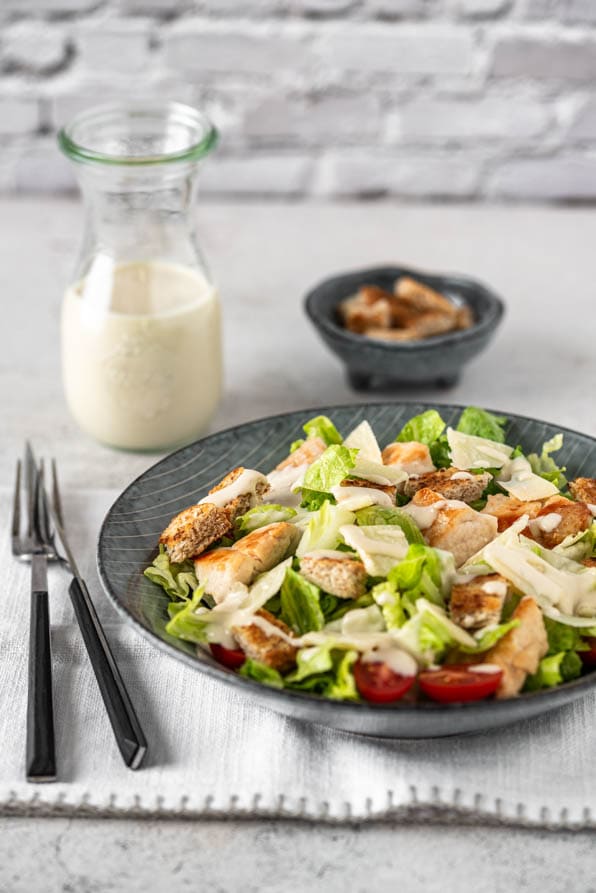 Eine Bowl Caesar Salad mit Besteck, Dressing und Croutons