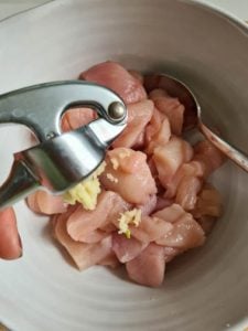 Hand presst Knoblauch in Schüssel mit Hähnchen