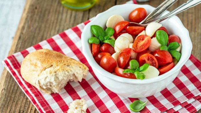 Ein Schälchen Tomaten Mozzarella Salat mit Baguette und Basilikumstrauch