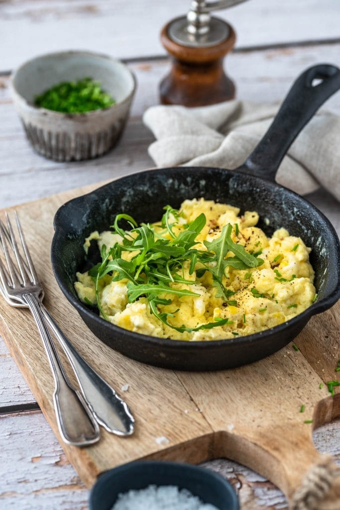 Ein Pfännchen Rührei auf einem Brett mit Besteck.