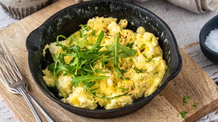 Ein Pfännchen Rührei auf einem Brett mit Besteck.