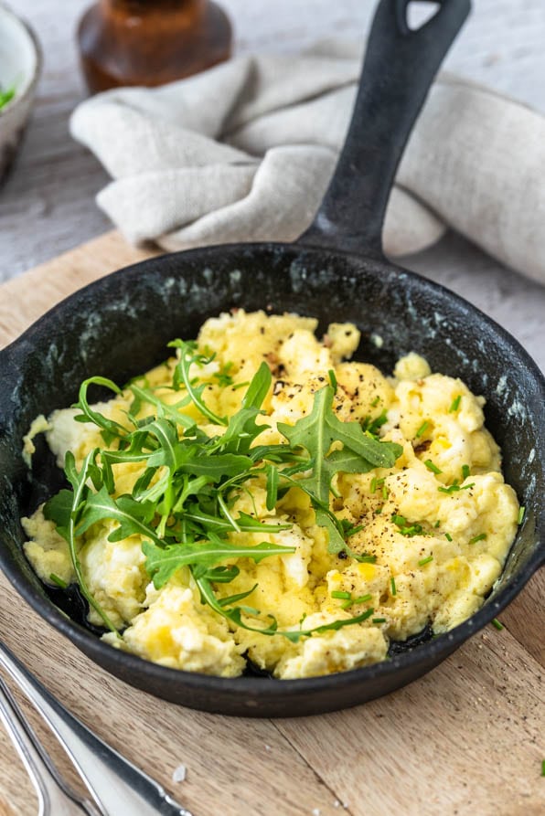 Ein Pfännchen Rührei auf einem Brett mit Besteck.