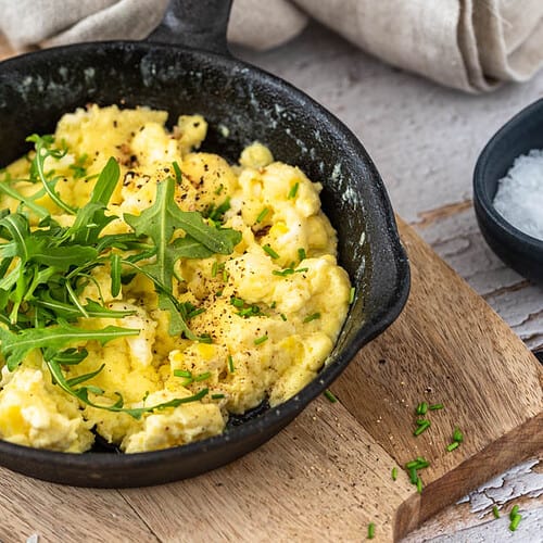 Ein Pfännchen Rührei auf einem Brett mit Besteck.