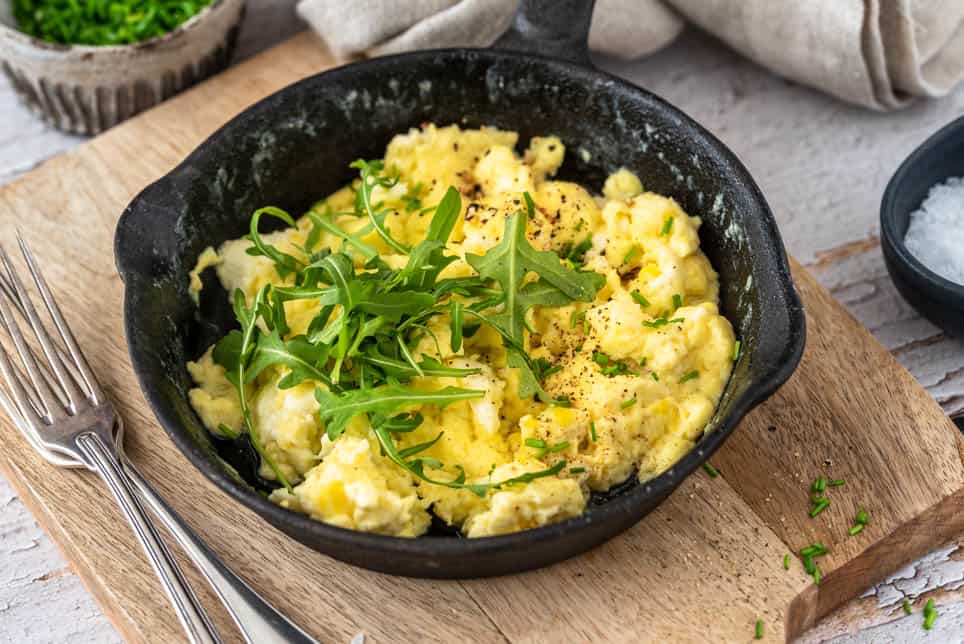 Ein Pfännchen Rührei auf einem Brett mit Besteck.