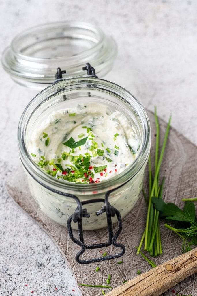 Ein Einmachglas mit Kräuterquark und gehackten Kräutern als Beilage zu Bratlinge