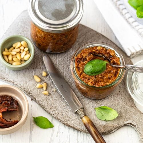 Pesto Rosso in Gläsern auf Schneidebrett mit Pinienkernen und Basilikum