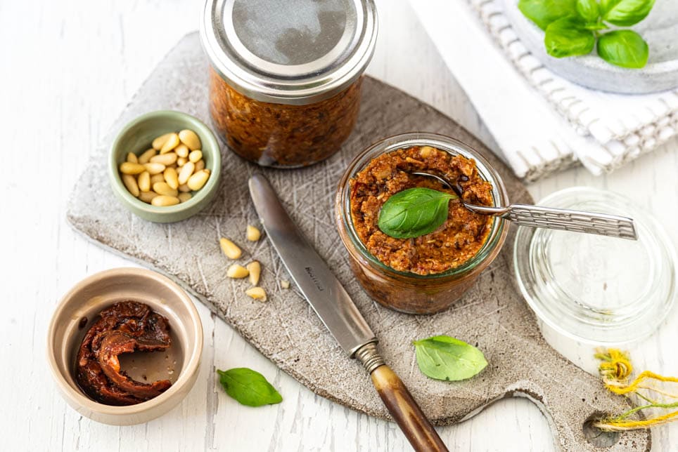 Pesto Rosso in Gläsern auf Schneidebrett mit Pinienkernen und Basilikum