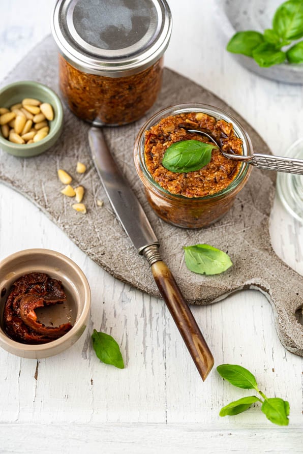 Pesto Rosso in Gläsern auf Schneidebrett mit Pinienkernen und Basilikum