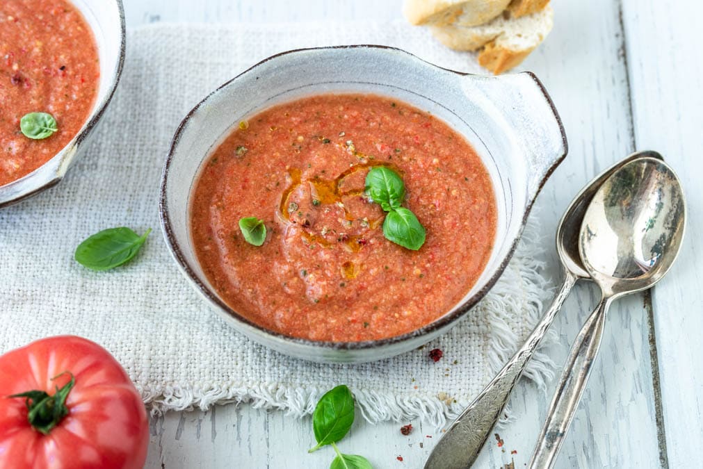 Zwei Schalen mit Gazpacho andaluz mit Baguettescheiben und Tomaten