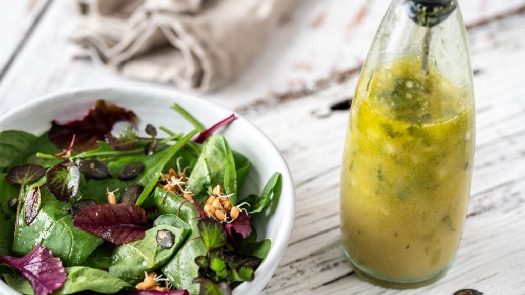 Vinaigrette in einer Flasche mit Blattsalat auf einem Holzuntergrund
