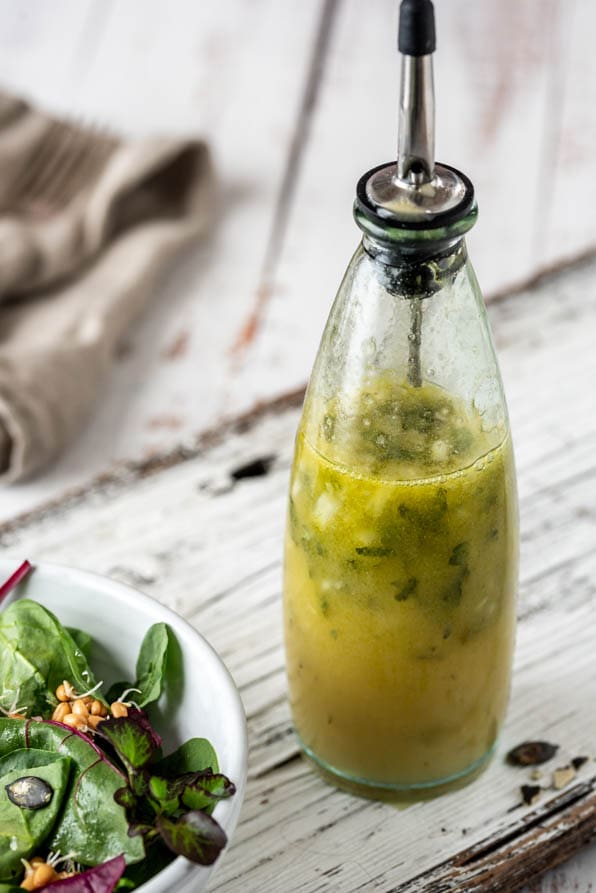 Vinaigrette in einer Flasche mit Blattsalat auf einem Holzuntergrund