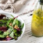 Vinaigrette in einer Flasche mit Blattsalat auf einem Holzuntergrund