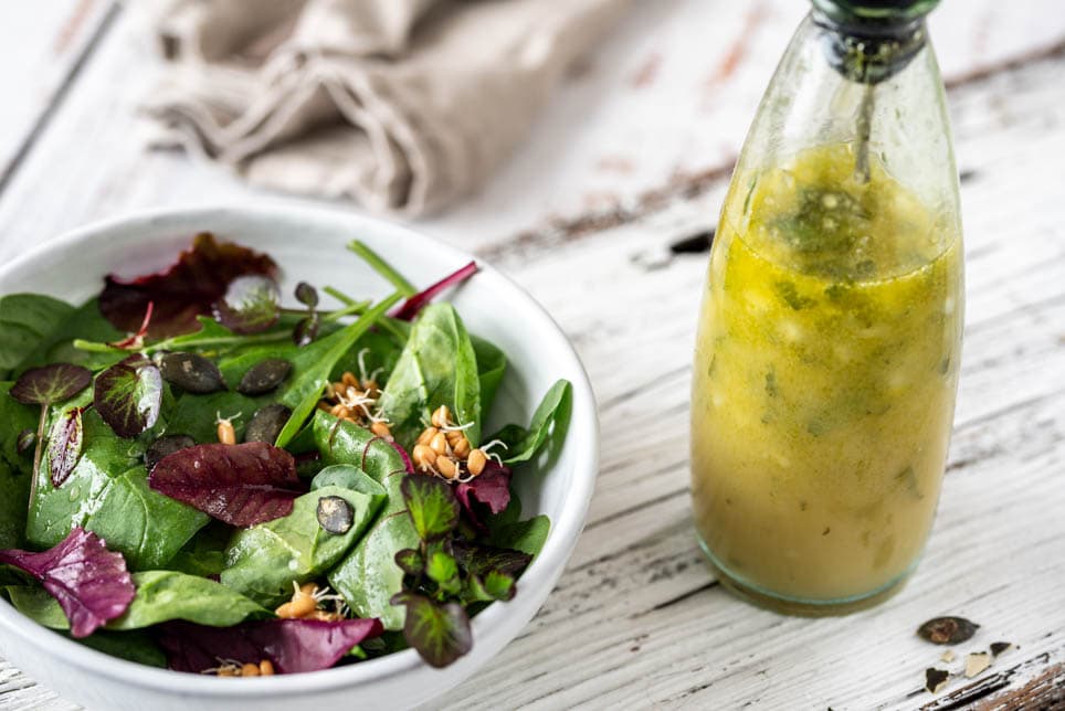 Vinaigrette in einer Flasche mit Blattsalat auf einem Holzuntergrund