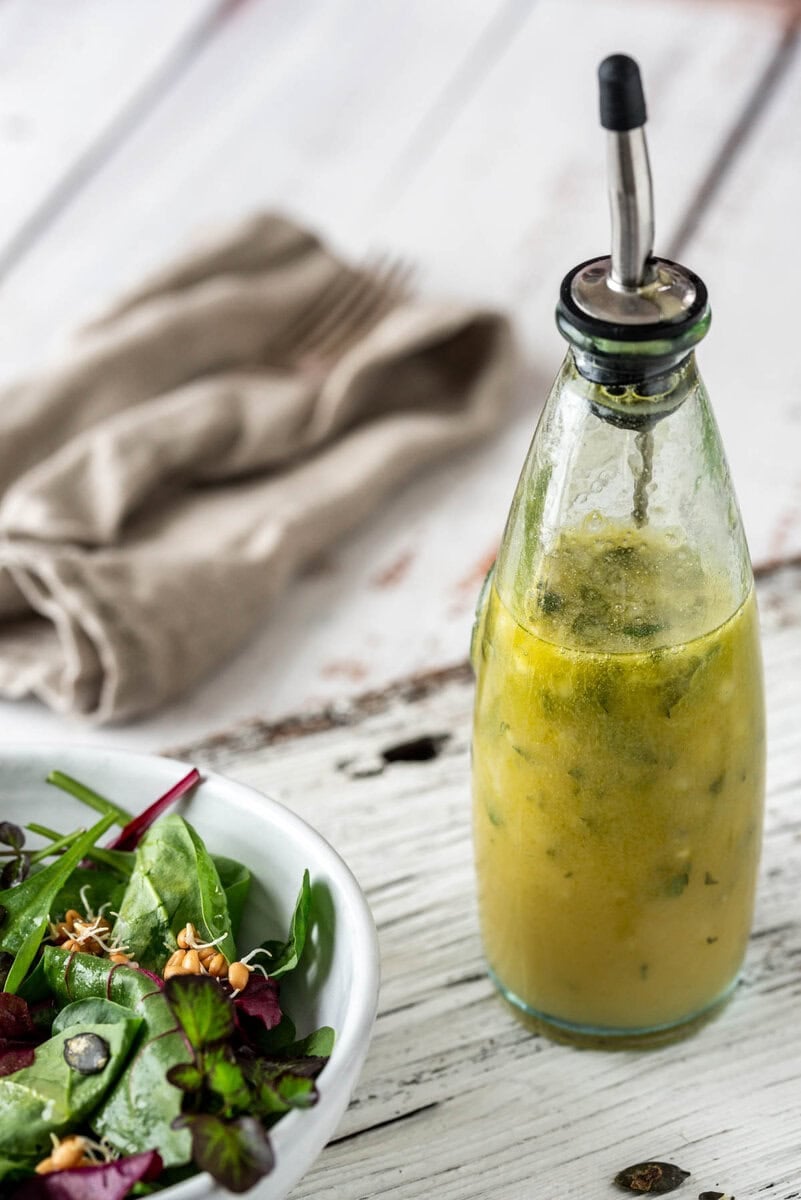 Vinaigrette in einer Flasche mit Blattsalat auf einem Holzuntergrund