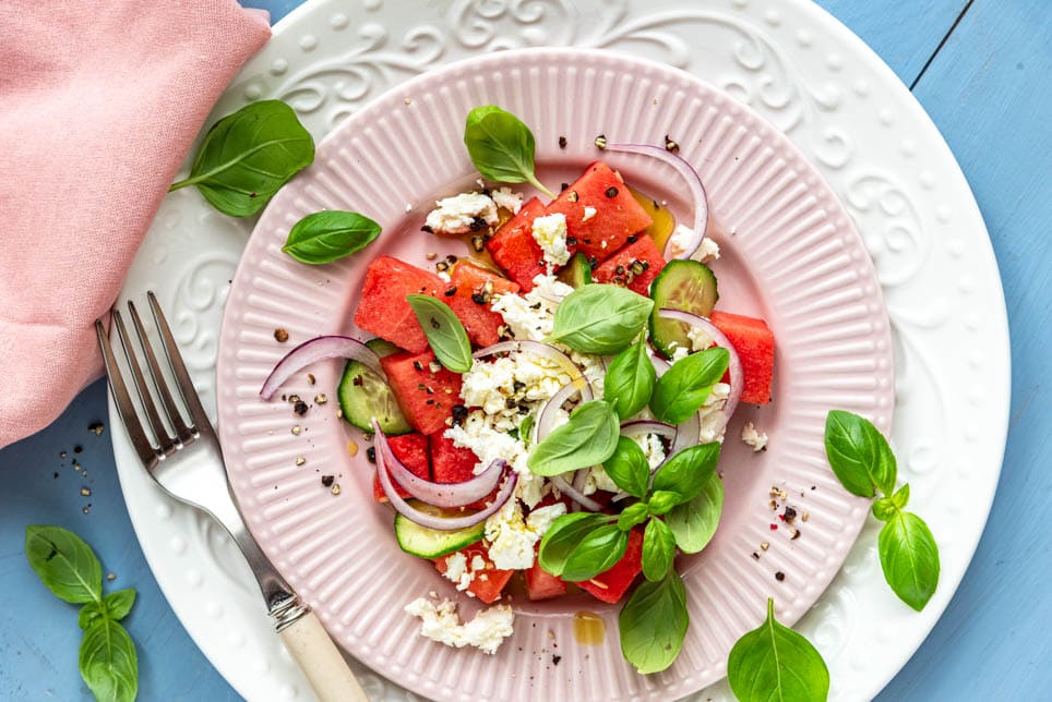 Wassermelonensalat mit Feta auf Tellern angerichtet und mit Basilikum garniert