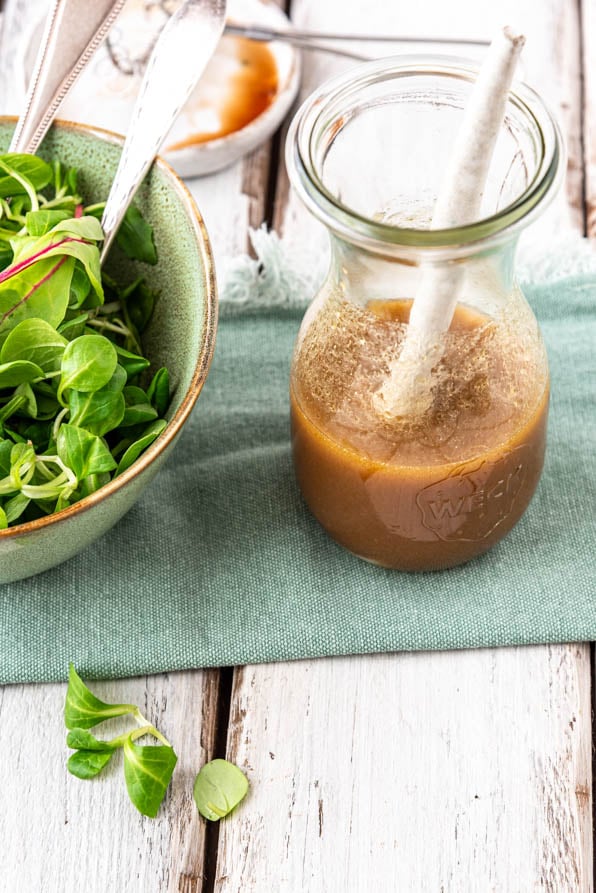 Ein Glas mit Balsamico Dressing und eine Schüssel Blattsalat.