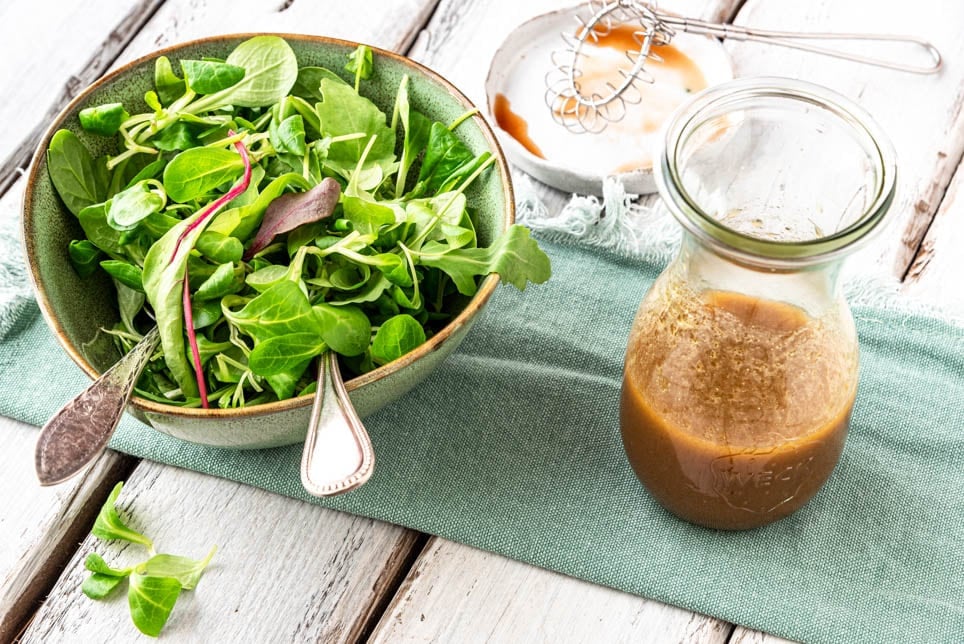 Ein Glas mit Balsamico Dressing und eine Schüssel Blattsalat.