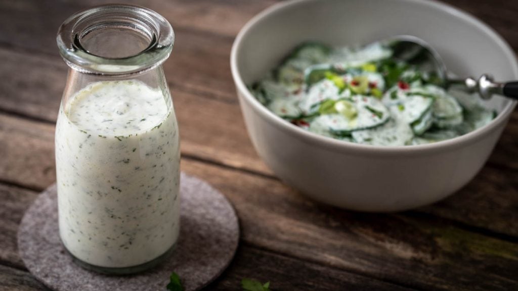 Joghurt Dressing in einem Glas, daneben Gurkensalat