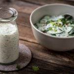Joghurt Dressing in einem Glas, daneben Gurkensalat