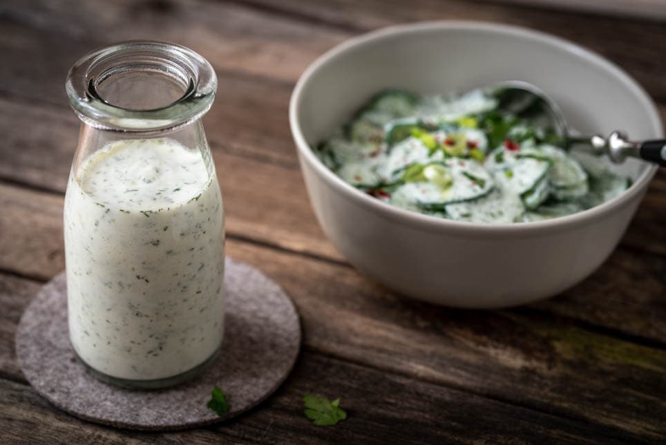 Joghurt Dressing in einem Glas, daneben Gurkensalat