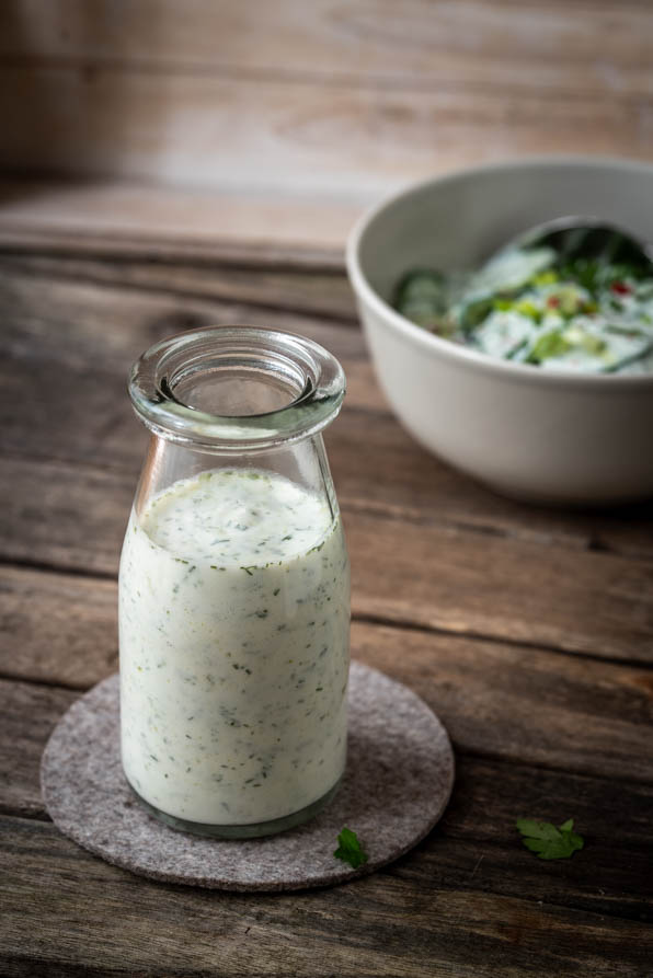 Joghurt Dressing in einem Glas, daneben Gurkensalat
