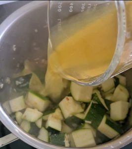 Gemüsebrühe wird zu Zucchini in Kochtopf gegossen