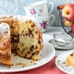 Angeschnittener Apfel-Gugelhupf mit Tassen und Äpfeln auf Tisch