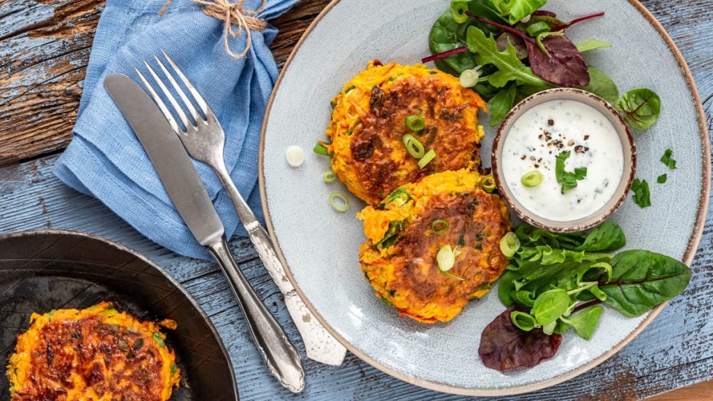 Kürbispuffer mit Salat und Dip auf einem Teller. Daneben eine Pfanne - Foodblog Mundgefühl