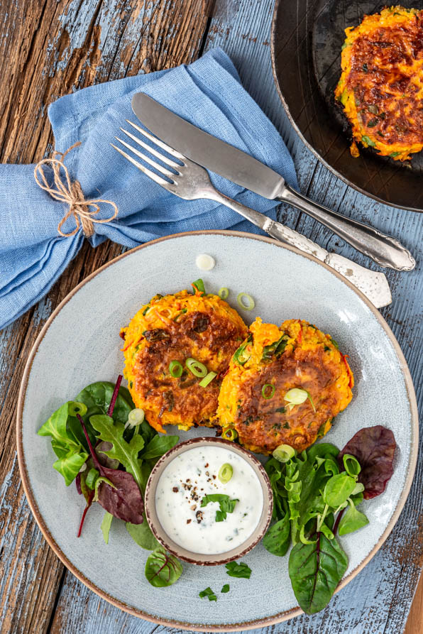 Kürbispuffer mit Salat und Dip auf einem Teller. Daneben eine Pfanne - Foodblog Mundgefühl
