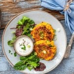 Kürbispuffer mit Salat und Dip auf einem Teller. Daneben eine Pfanne - Foodblog Mundgefühl