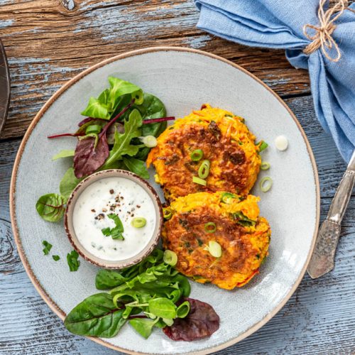 Kürbispuffer mit Salat und Dip auf einem Teller. Daneben eine Pfanne - Foodblog Mundgefühl