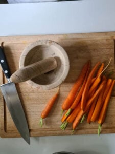Karotten mit Grün liegen auf Schneidebrett. Daneben ein Mörser