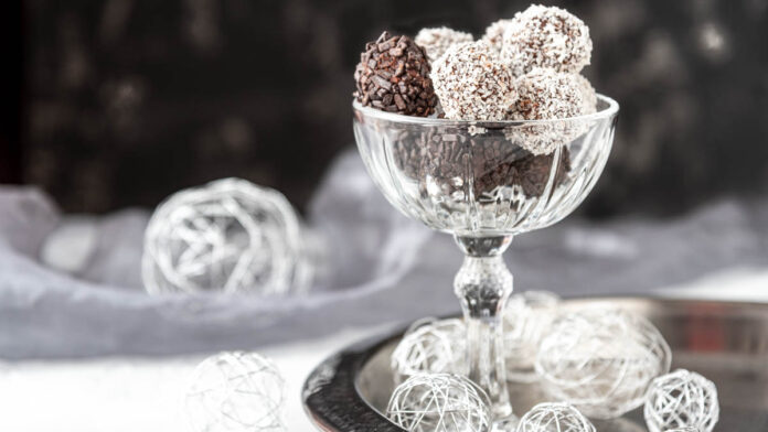 rumkugeln-selber-machen-einfach-und-schnell Schokoladige Rumkugeln in einer eleganten Glasschale, mit Kokos und Schokostreuseln umhüllt, festlich angerichtet auf einem silbernen Tablett