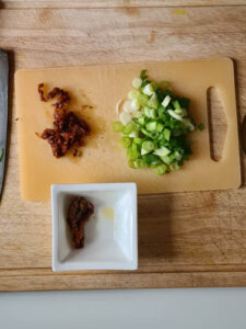 Geschnittener Lauchzwiebel und Tomaten in Öl auf Holzbrett