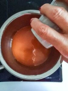 Hand gießt Flüssigkeit in Kochtopf für Hot Aperol Rezept