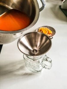Flüssigkeit wird aus Kochtopf in Glas gekippt für Hot Aperol Rezept