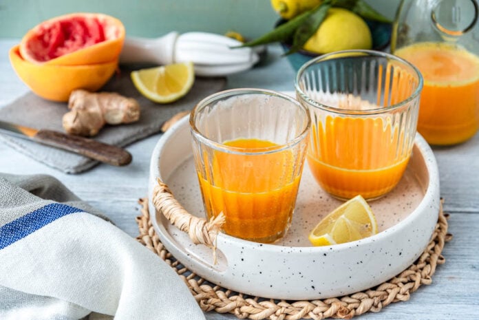 Zwei Gläser Ingwer Shot auf Tablett mit Grapefruits