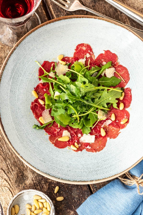 Ein Teller Carpaccio steht mit Wein auf Holzuntergrund - Foodblog Mundgefühl
