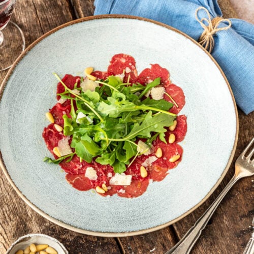 Klassisches Carpaccio auf Holzuntergrund mit Besteck